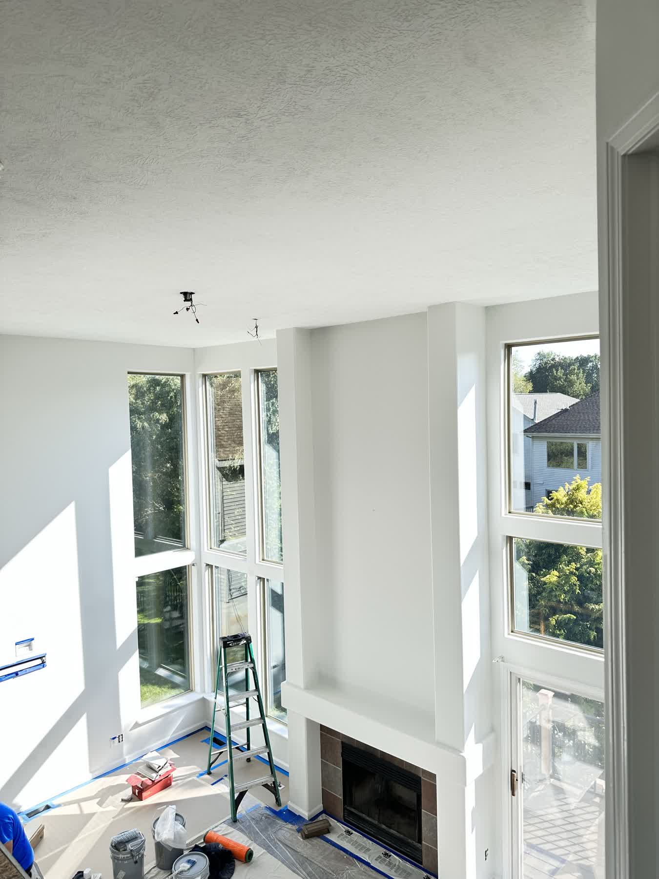Double-height residential great room with fresh white paint, fireplace, and tall windows